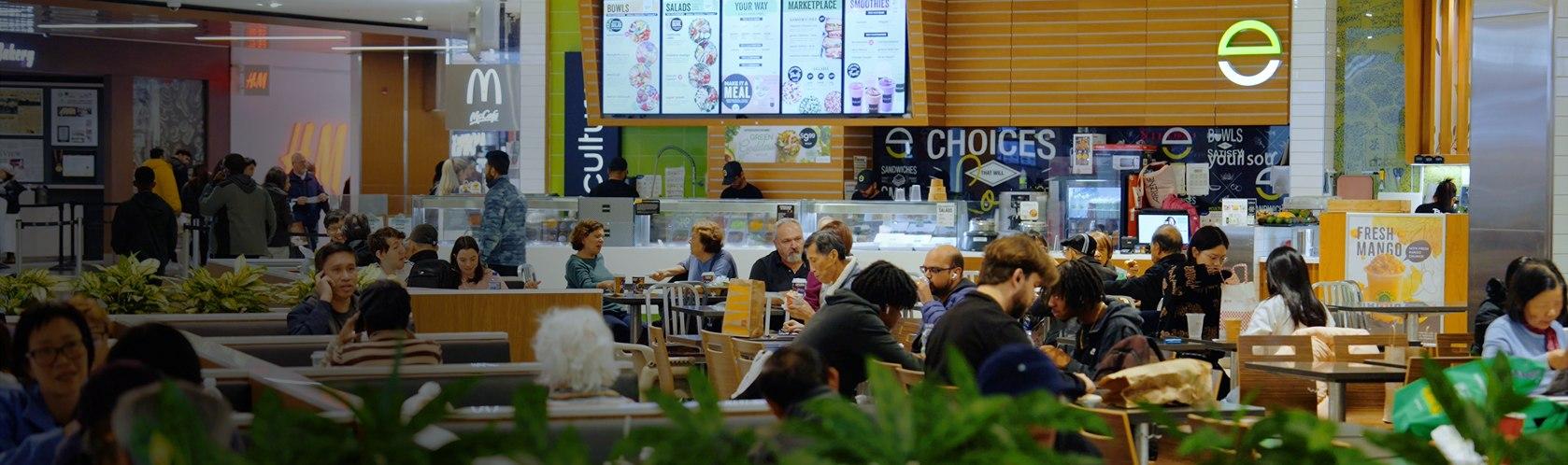 Busy food court area with people dining and ordering from a variety of food vendors