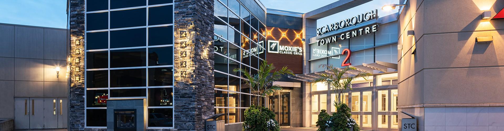 Exterior of Scarborough Town Centre entrance with modern architecture and storefront signage at dusk