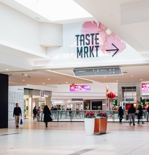 Shoppers walking through a shopping centre corridor past Winners and Swarovski stores with displays