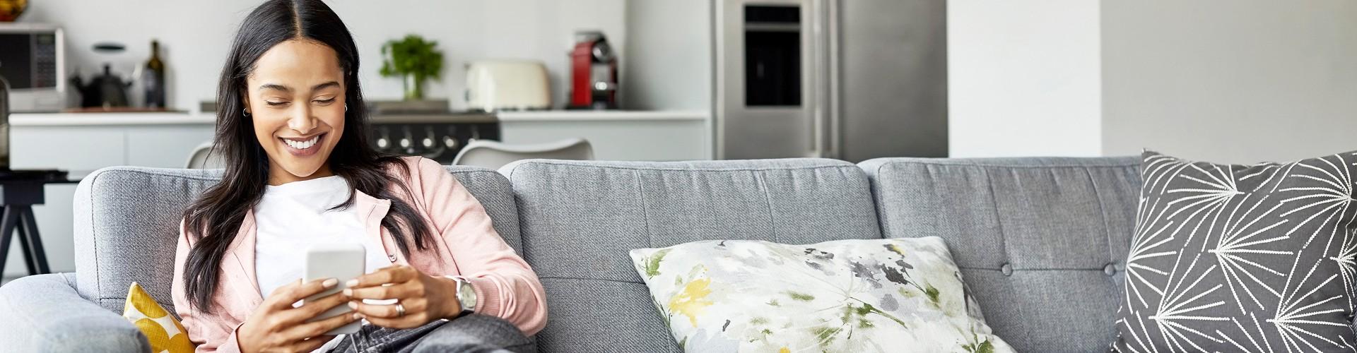 Woman relaxing on a sofa at home while browsing a gift card on her phone in a comfortable setting