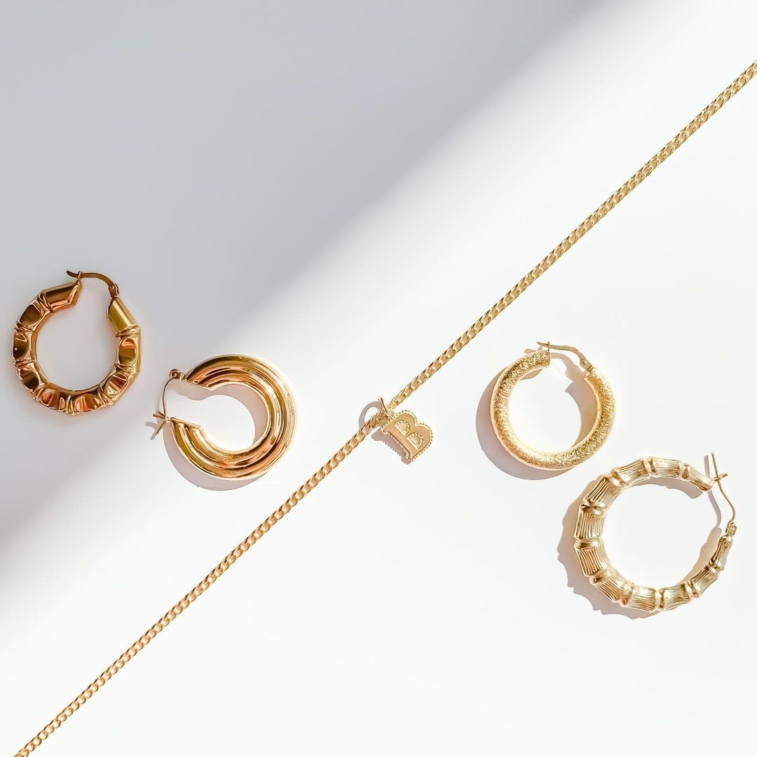 Three pieces of gold jewellery. On the left are two small gold hoops. In the middle is a gold chain necklace with a 'B' pendant. On the right are two medium sized gold hoops.