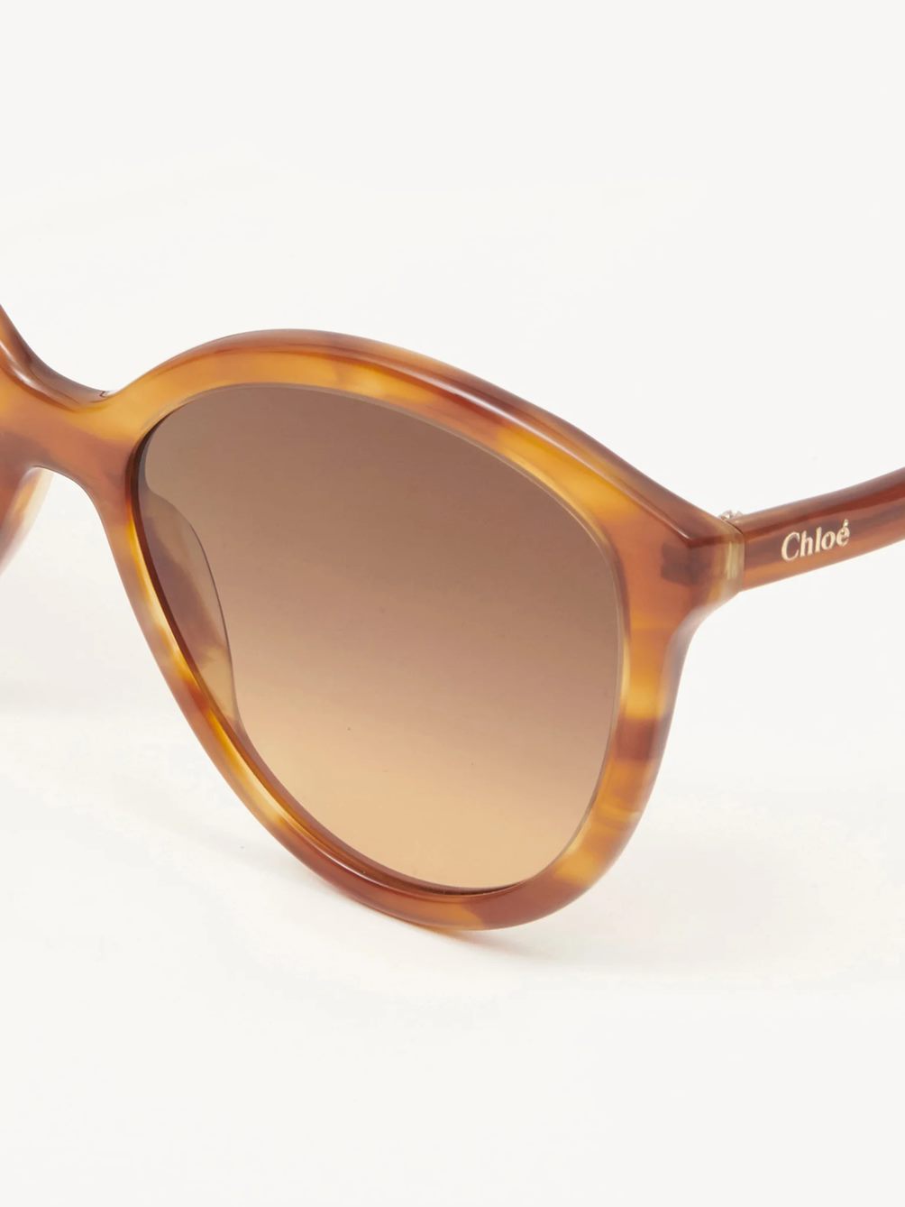 A close up of brown tortoise coloured sunglasses with a brown to cream ombre lens.
