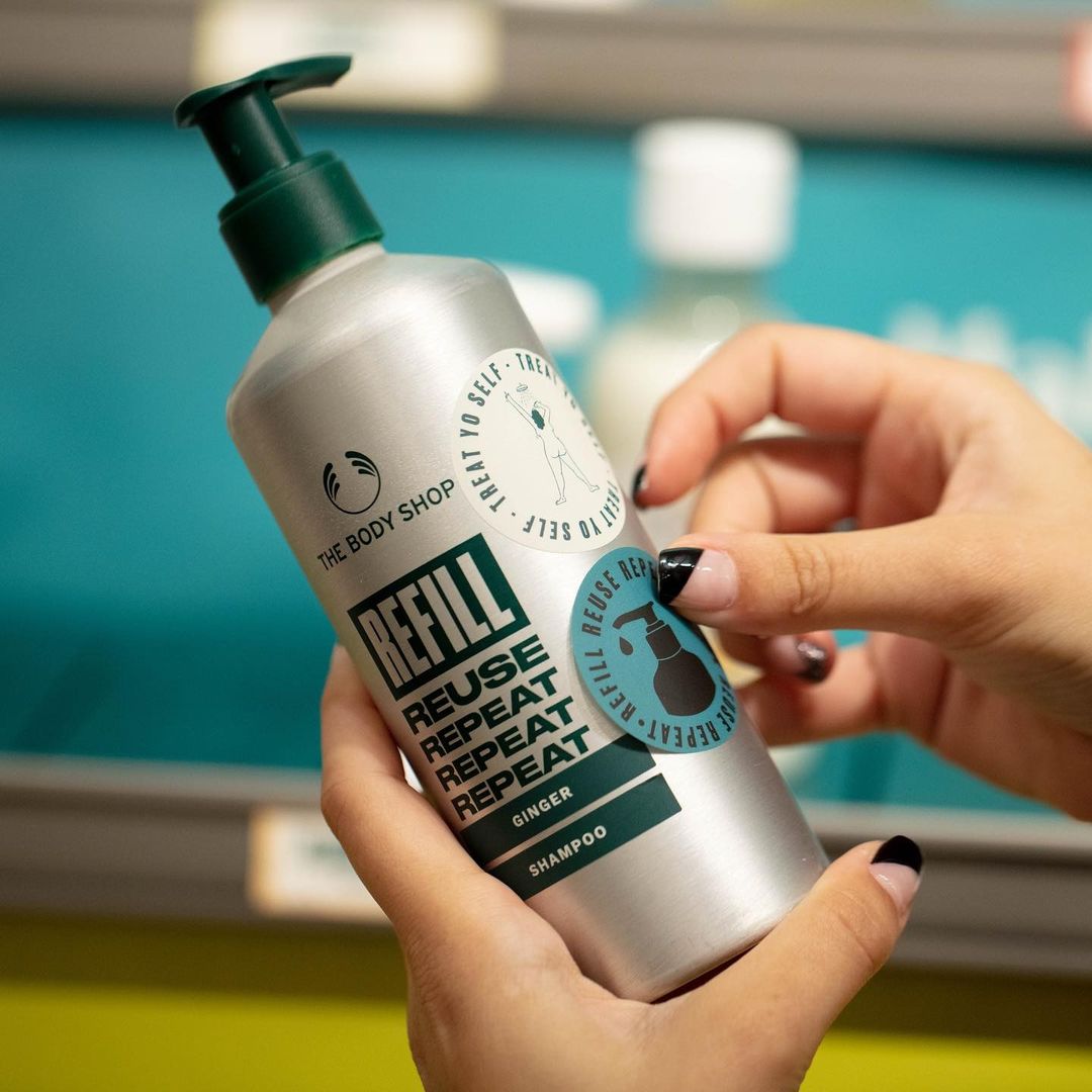 A person adding a blue label to a silver reusable shampoo bottle.