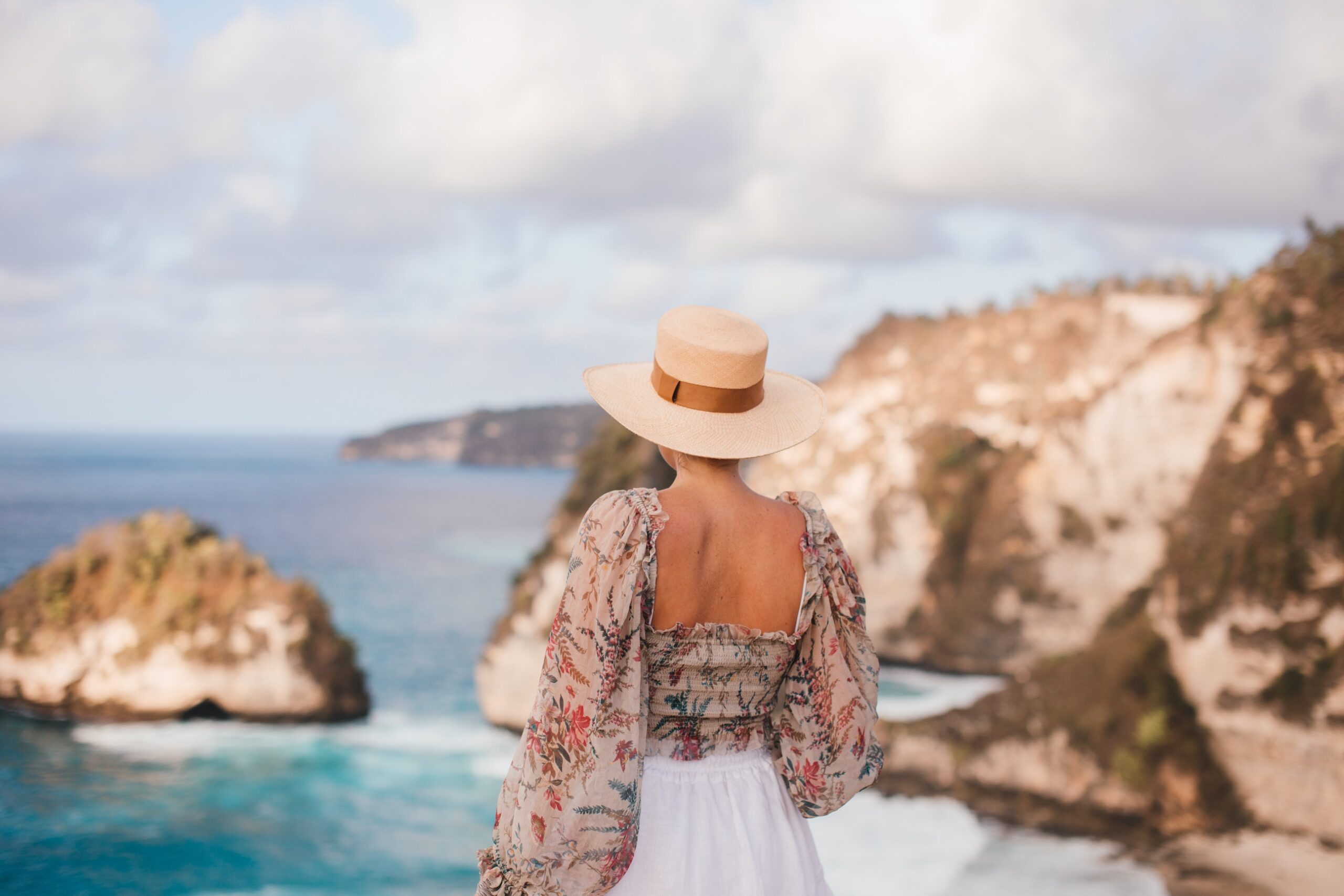 image of a woman wearing a straw hat and flowy top overlooking the ocean