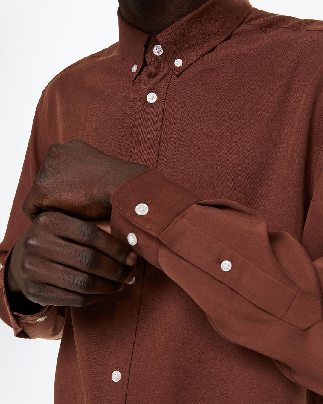 close-up image of model wearing a brown dress shirt with white buttons
