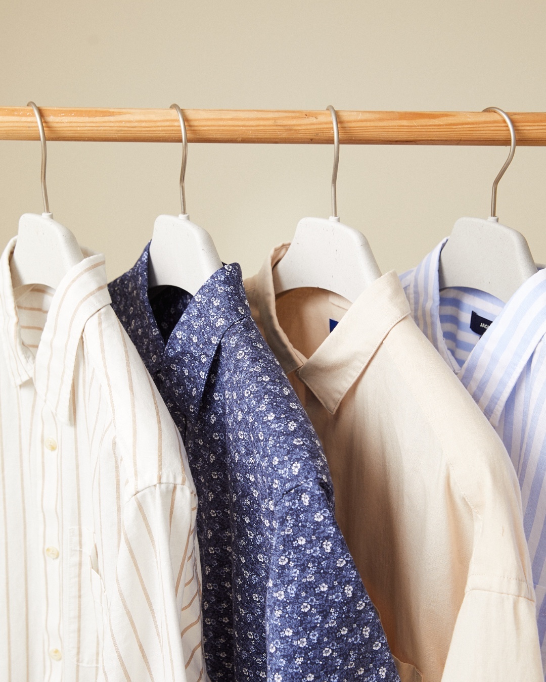 close-up image of four dress shirts hanging on hangers. they are white with pink stripes, paisley, peach and white with blue stripes