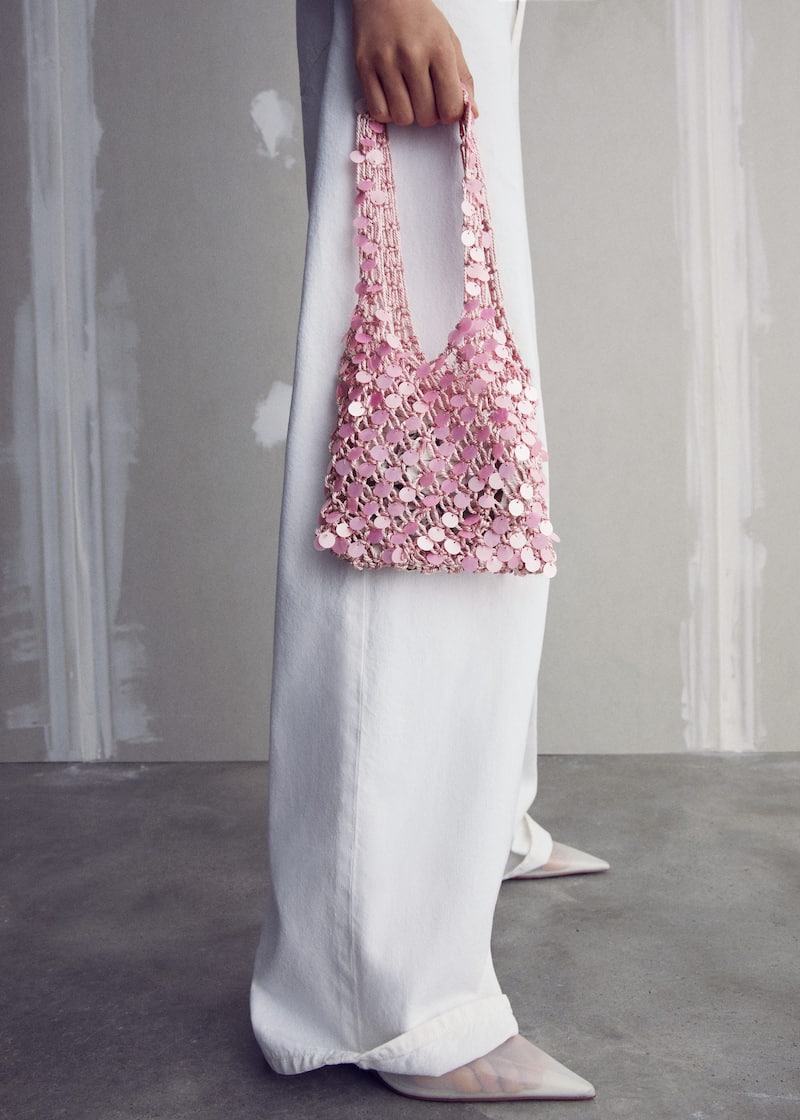 close-up image of a woman wearing baggy white pants and holding a pink sequinned handbag from MANGO