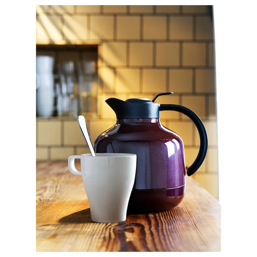 white coffee mug in front of a coffee pot on a wooden table