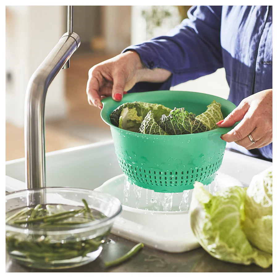 image of a woman washing vegetables in a green colander