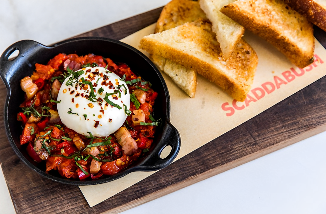 A skillet filled with a mozzarella ball and tomatoes accompanied by pieces of toasted focaccia