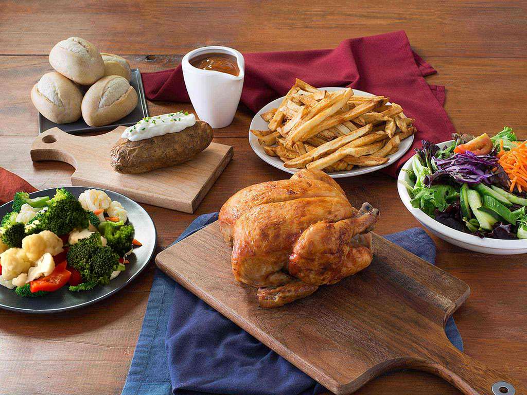 A spread of vegetables, fries, and a rotisserie chicken on a wooden table