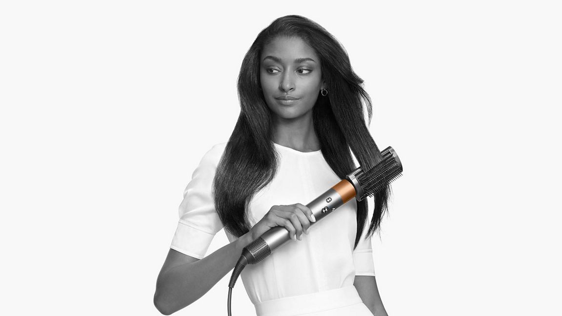 a person running a dyson hair brush dryer through her hair