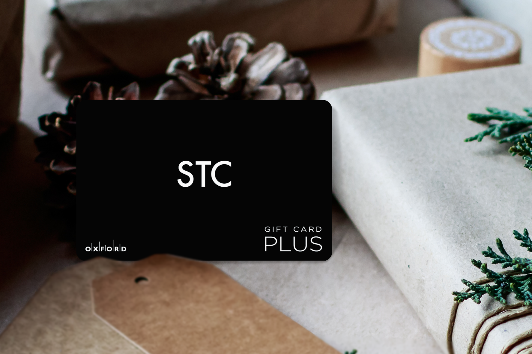 promotional image of a black STC gift card surrounded by gift-wrapped books in a holiday setting