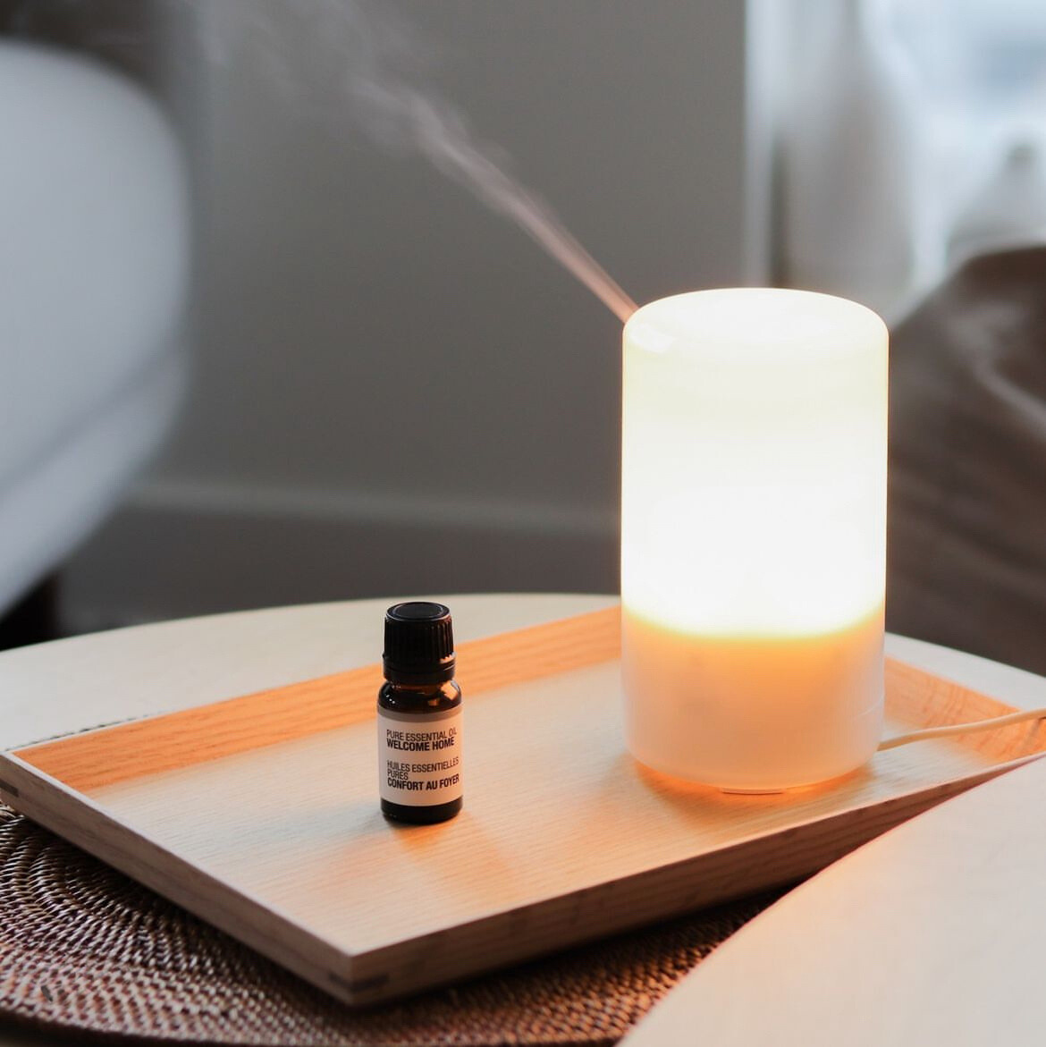 A wooden tray with a soft glow diffuser and essential oil resting on it.
