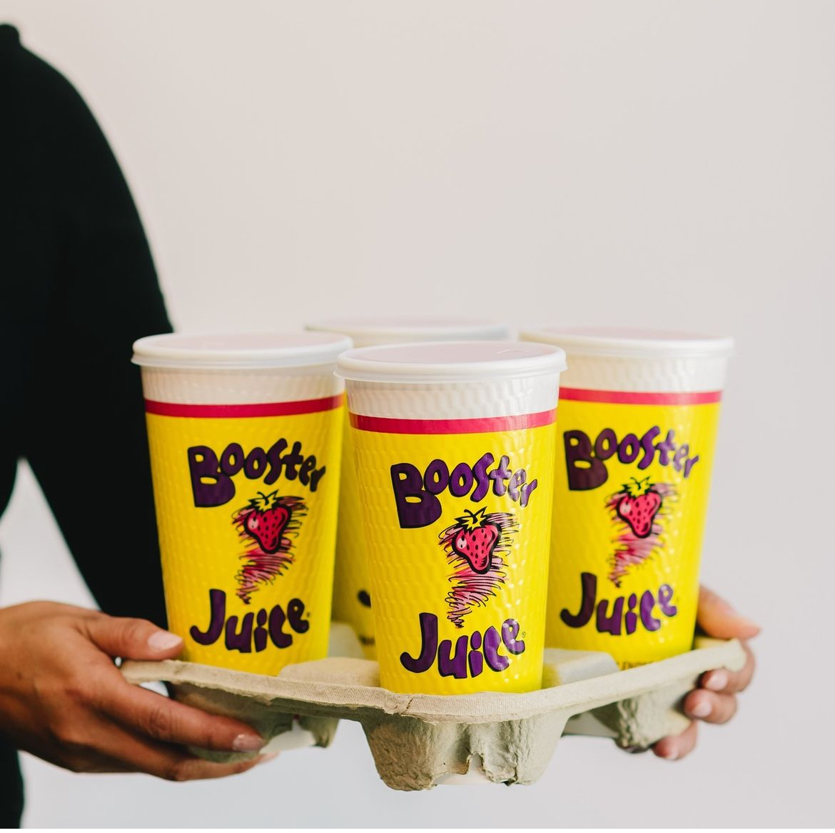 A person holding a tray of large take out smoothie cups