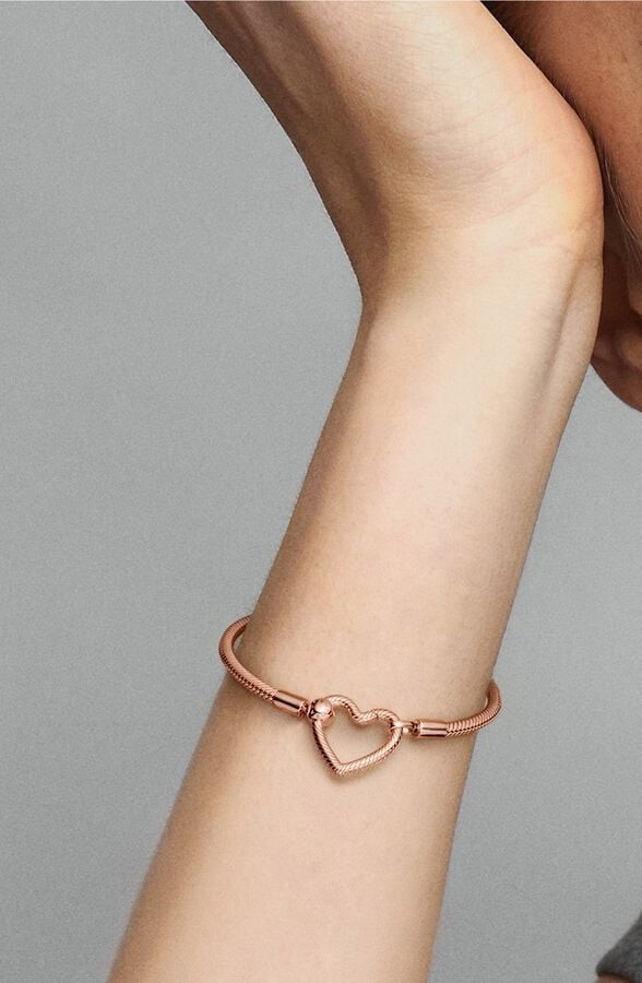 Wrist displaying a rose gold bracelet with large heart shaped charm