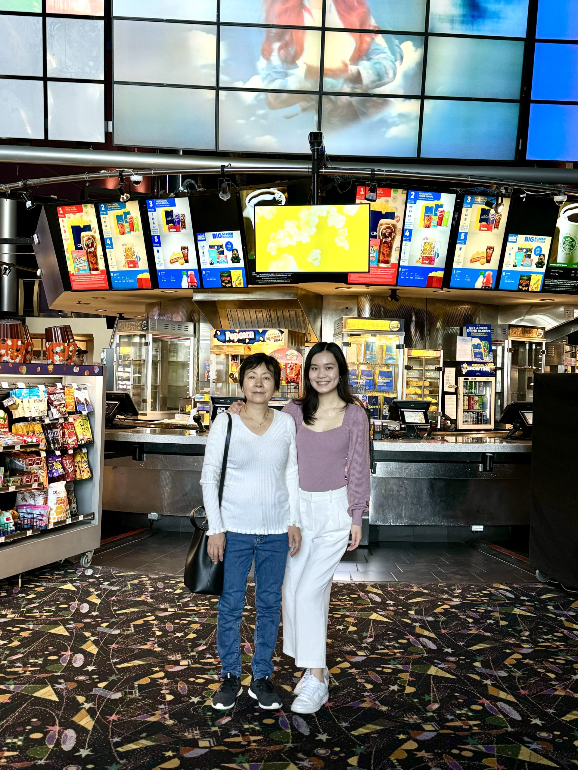 mother and daughter posing in front of movie theater concession stand
