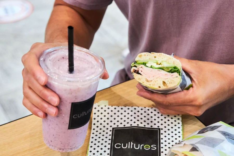 man holding a cultures smoothie and wrap