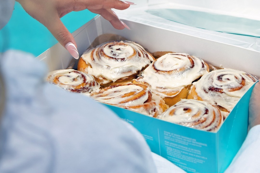 a lady holding half a dozen of cinnabons