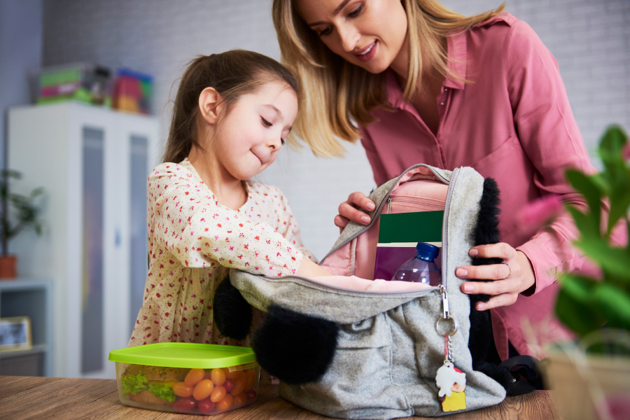 mother and daughter packing backpack for school