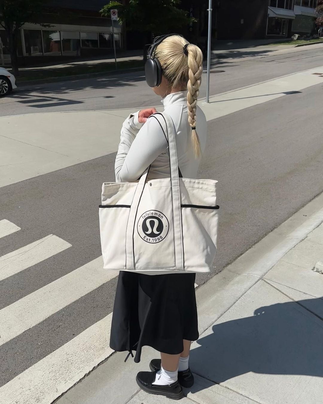 girl crossing the street holding white lululemon tote bag