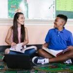 2 students sitting on the floor happily studying