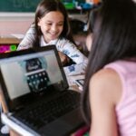 two girls talking in classroom with laptop