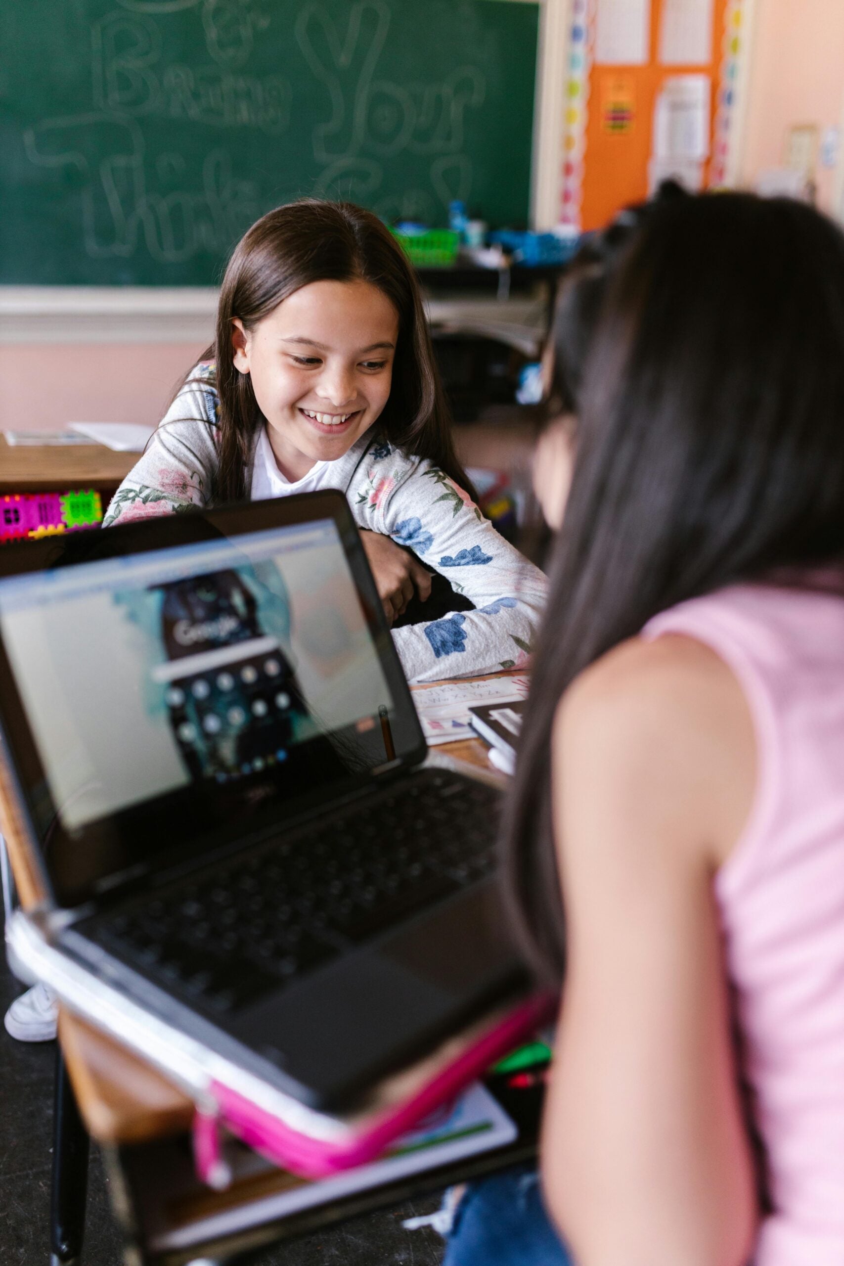 two girls talking in classroom with laptop