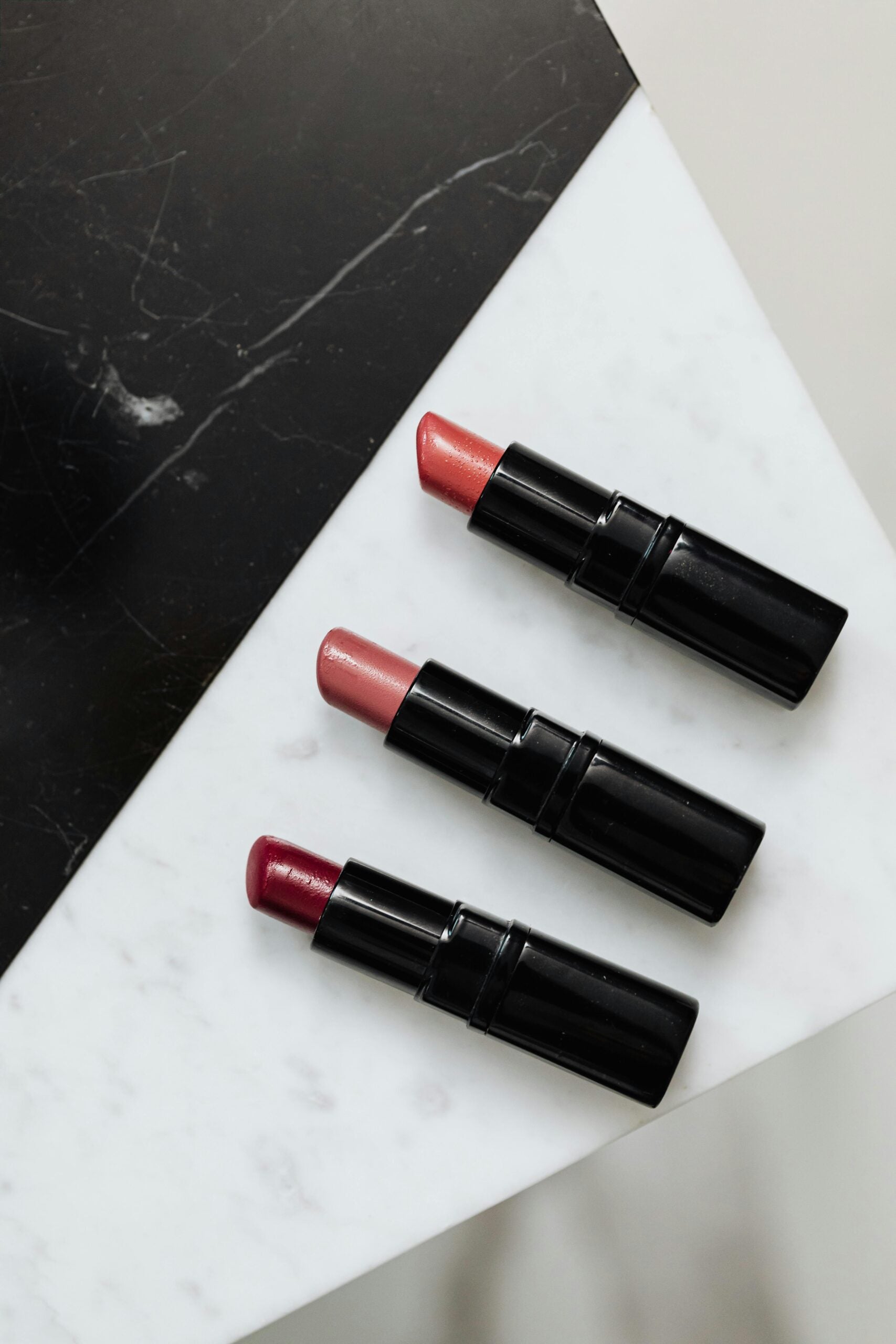 Three tubes of lipstick in various shades, on a white table.