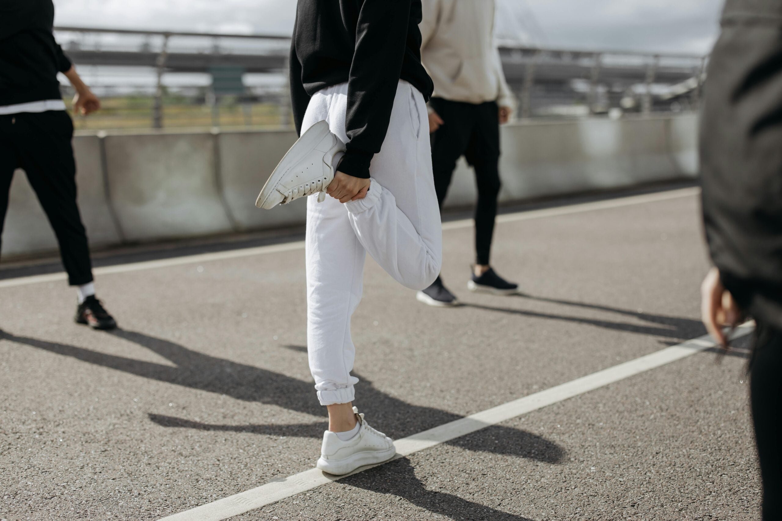 The bottom half of a person in white sweatpants, stretching.