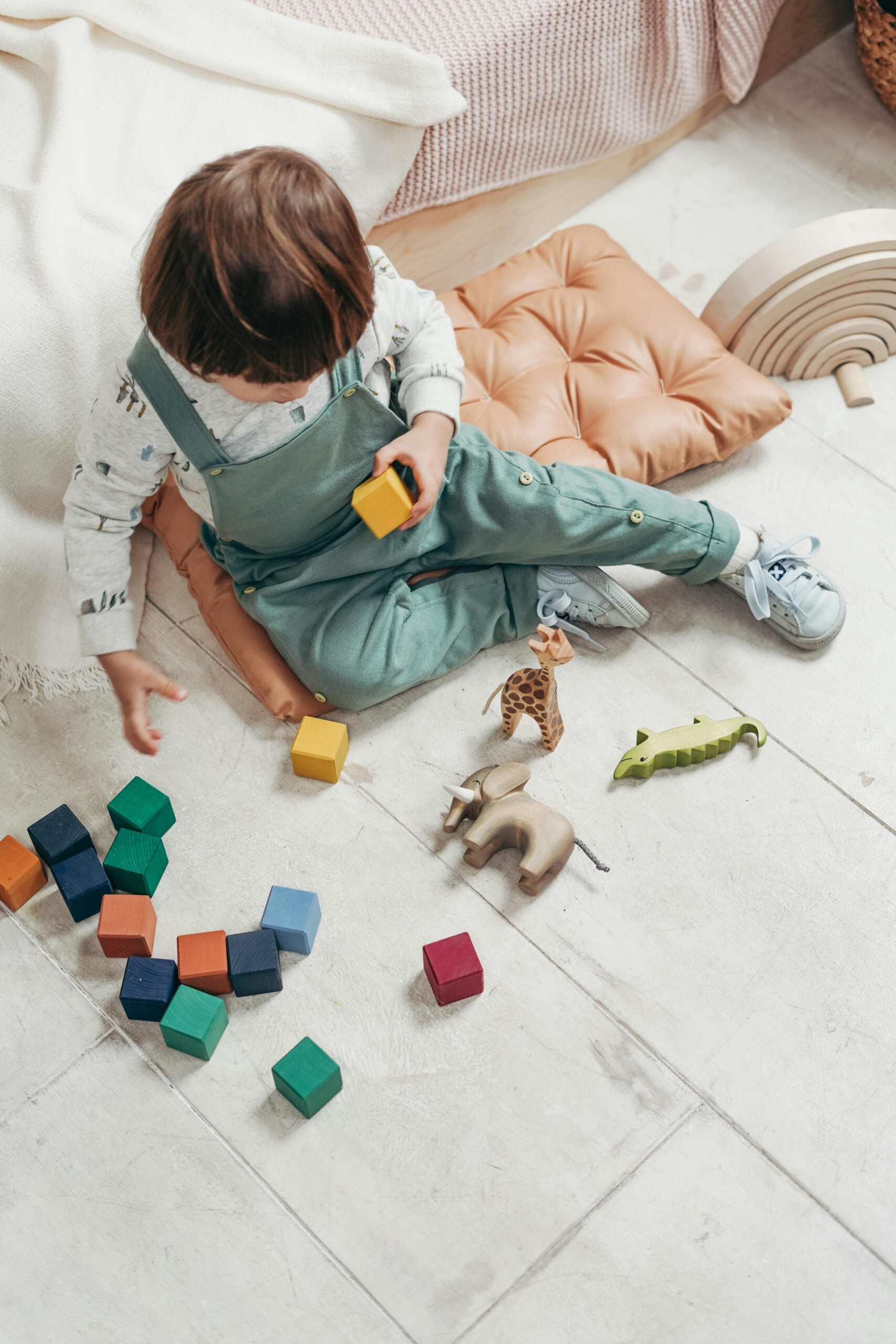 A child in overalls playing with toy blocks and toy animals.