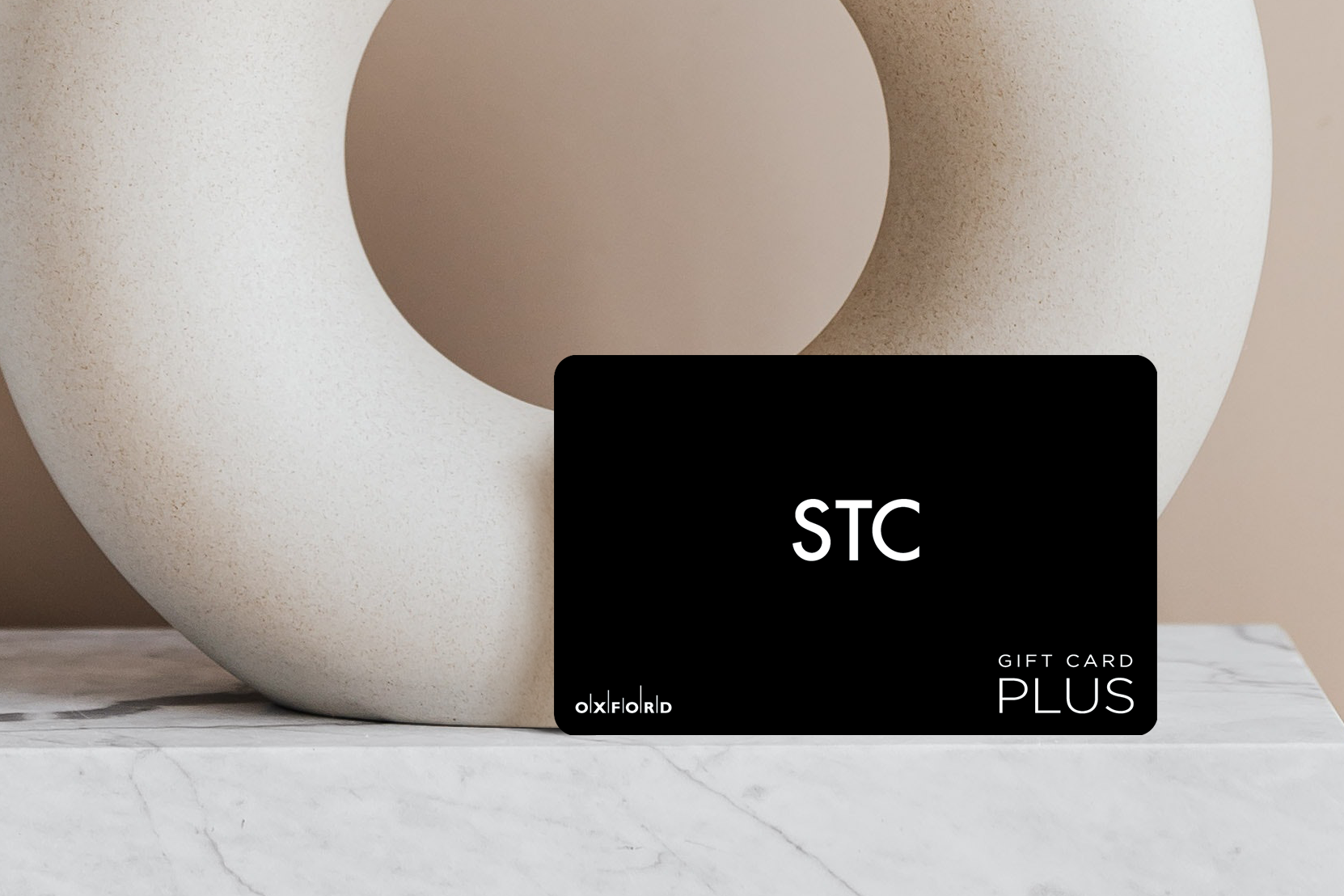 A black STC gift card leaning against a beige circular art piece.