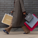 Woman with a textured brown coat holding shopping bags from Michael Kors and Coach.