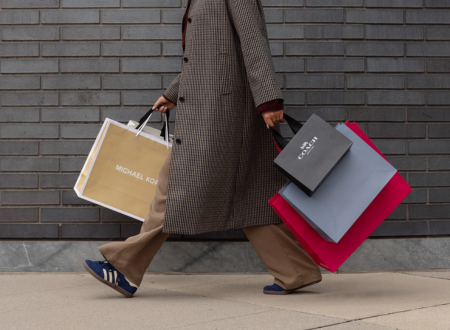 Woman with a textured brown coat holding shopping bags from Michael Kors and Coach.